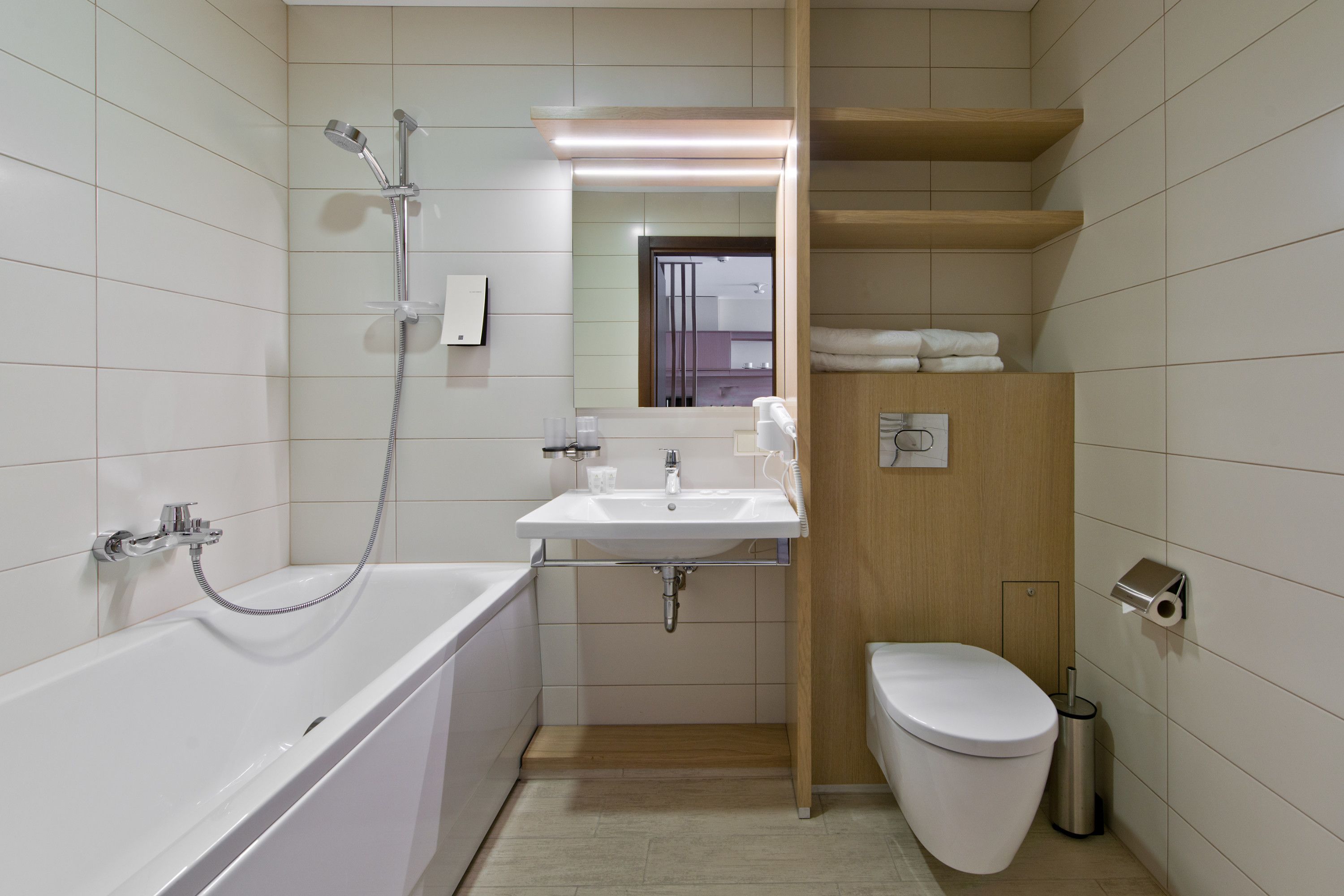A modern bathroom with a bathtub, sink, toilet, and wooden shelves.