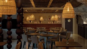 Restaurante com mesas e cadeiras redondas, luminárias de vime pendentes e teto de madeira.
