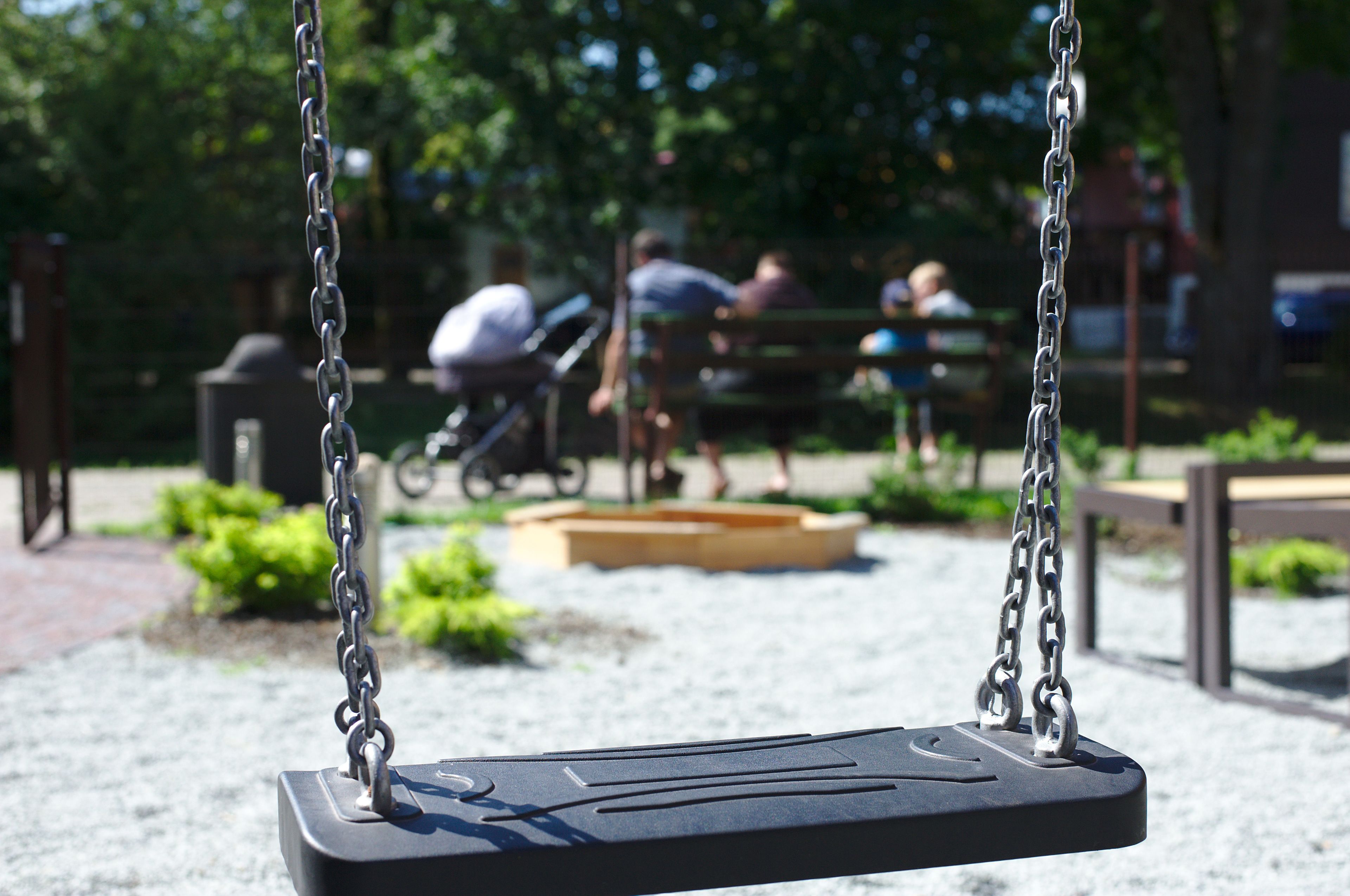 A park swing set with a metal chain and a black seat.