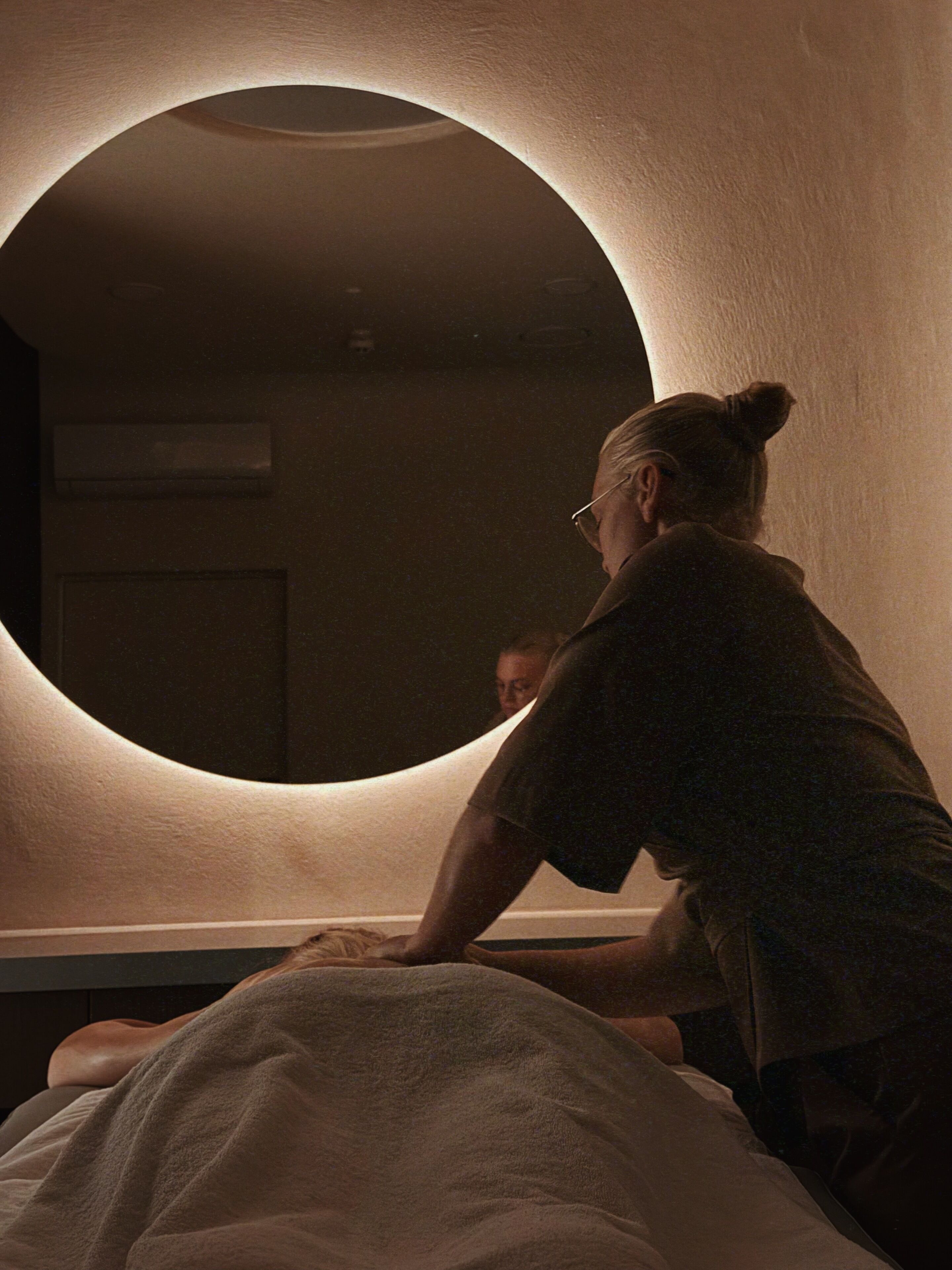 A person sitting on a bed with a circular mirror on the wall.