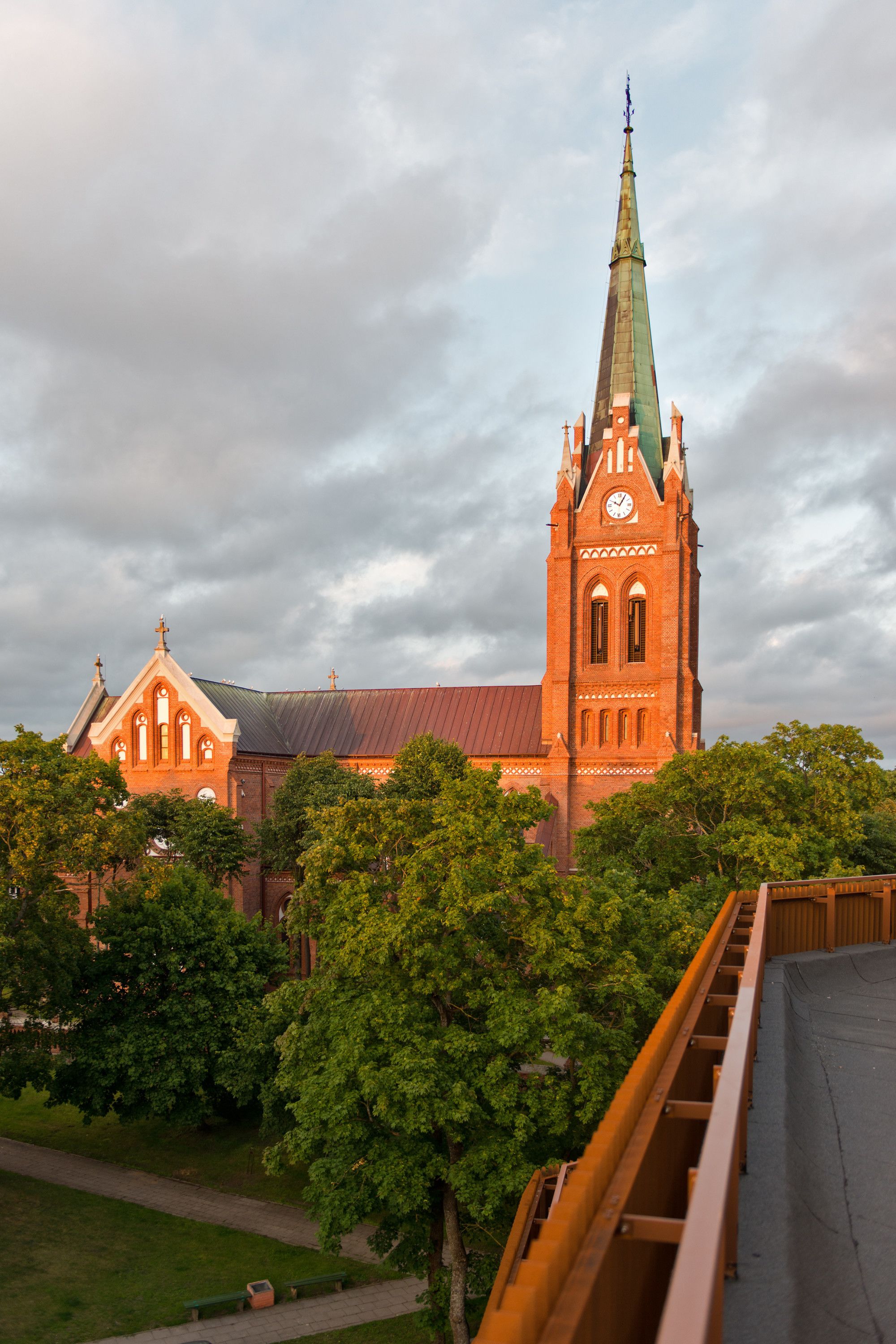 A church with a tall spire and a clock tower, surrounded by trees and a bridge.
