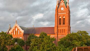 A church with a tall spire and a clock tower, surrounded by trees and a bridge.