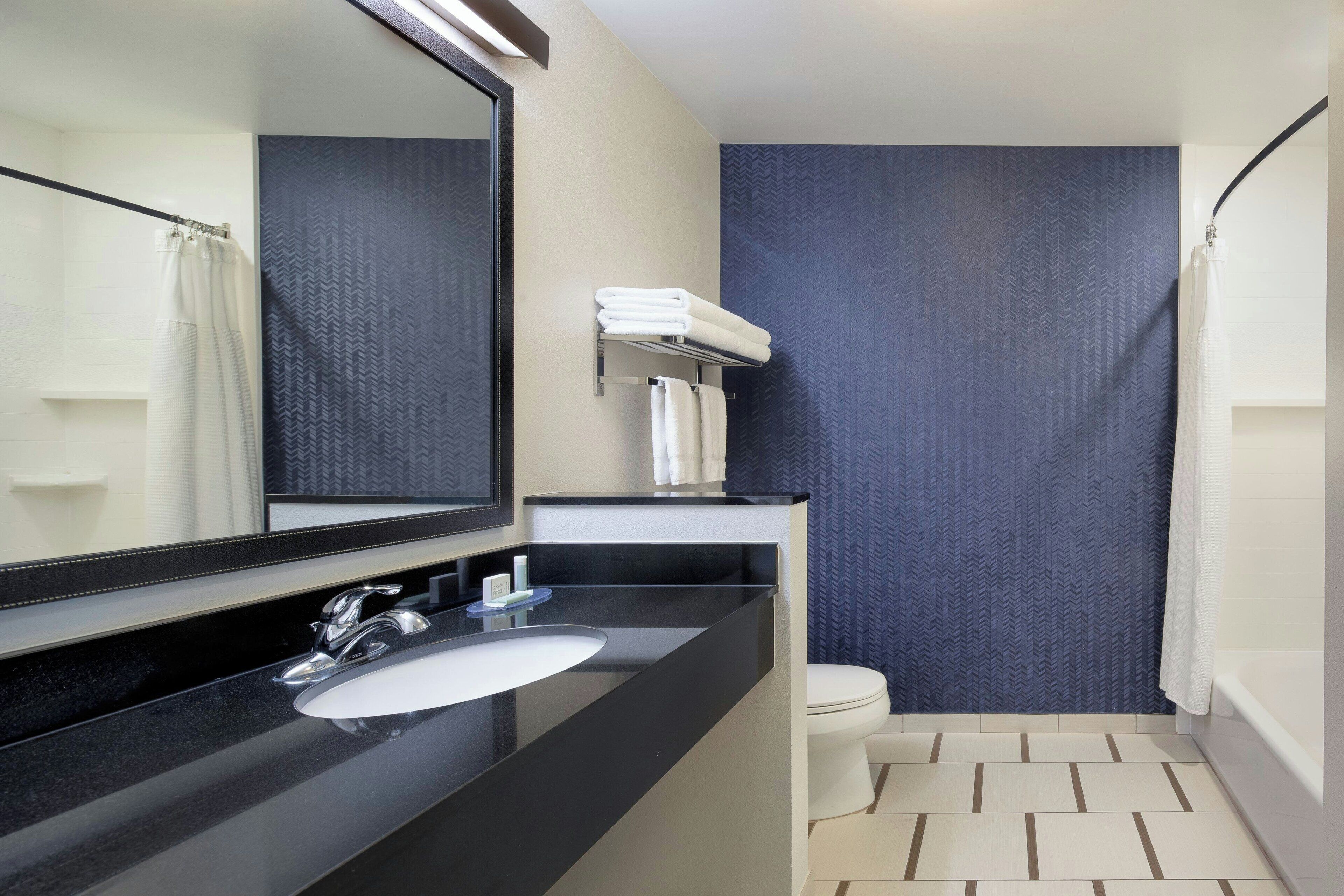 A modern bathroom with a black sink, a mirror, a white toilet, and a shower curtain.