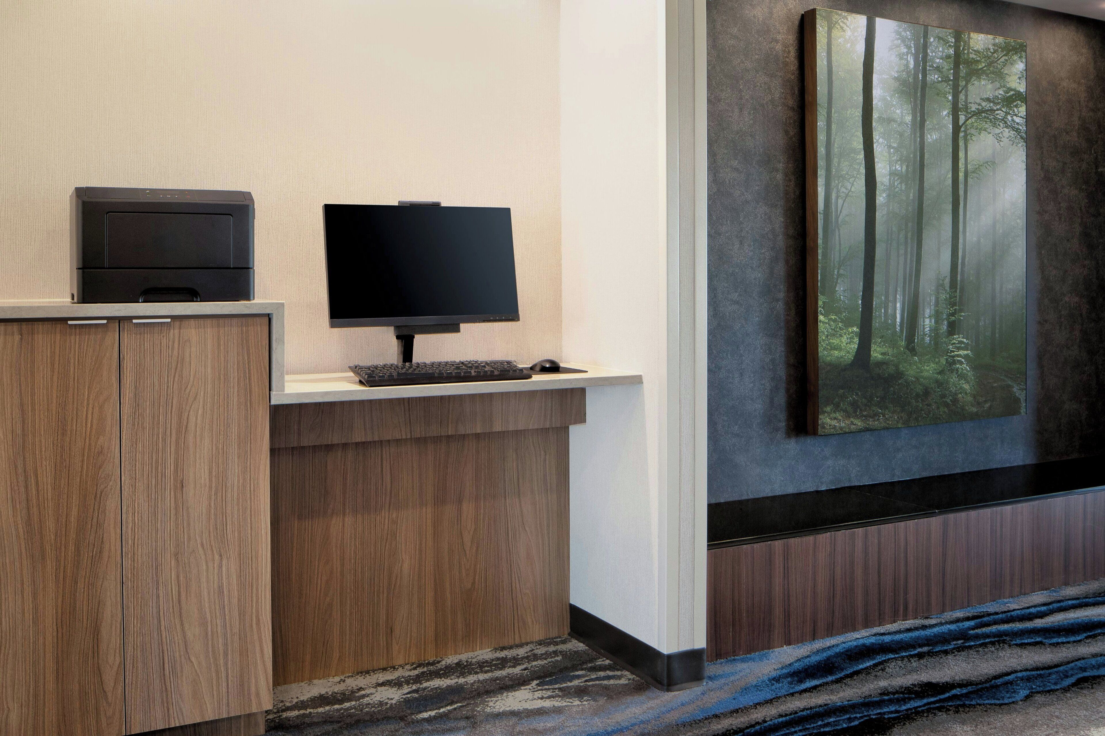 Ein Hotel-Rezeptionsbereich mit einem Holztisch, einem Flachbildfernseher, einem Drucker und einem großen Wandbild mit Waldmotiv.