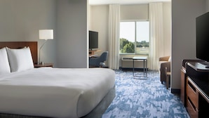 A hotel room with a large bed, a desk, a chair, a television, and a view of the outdoors.