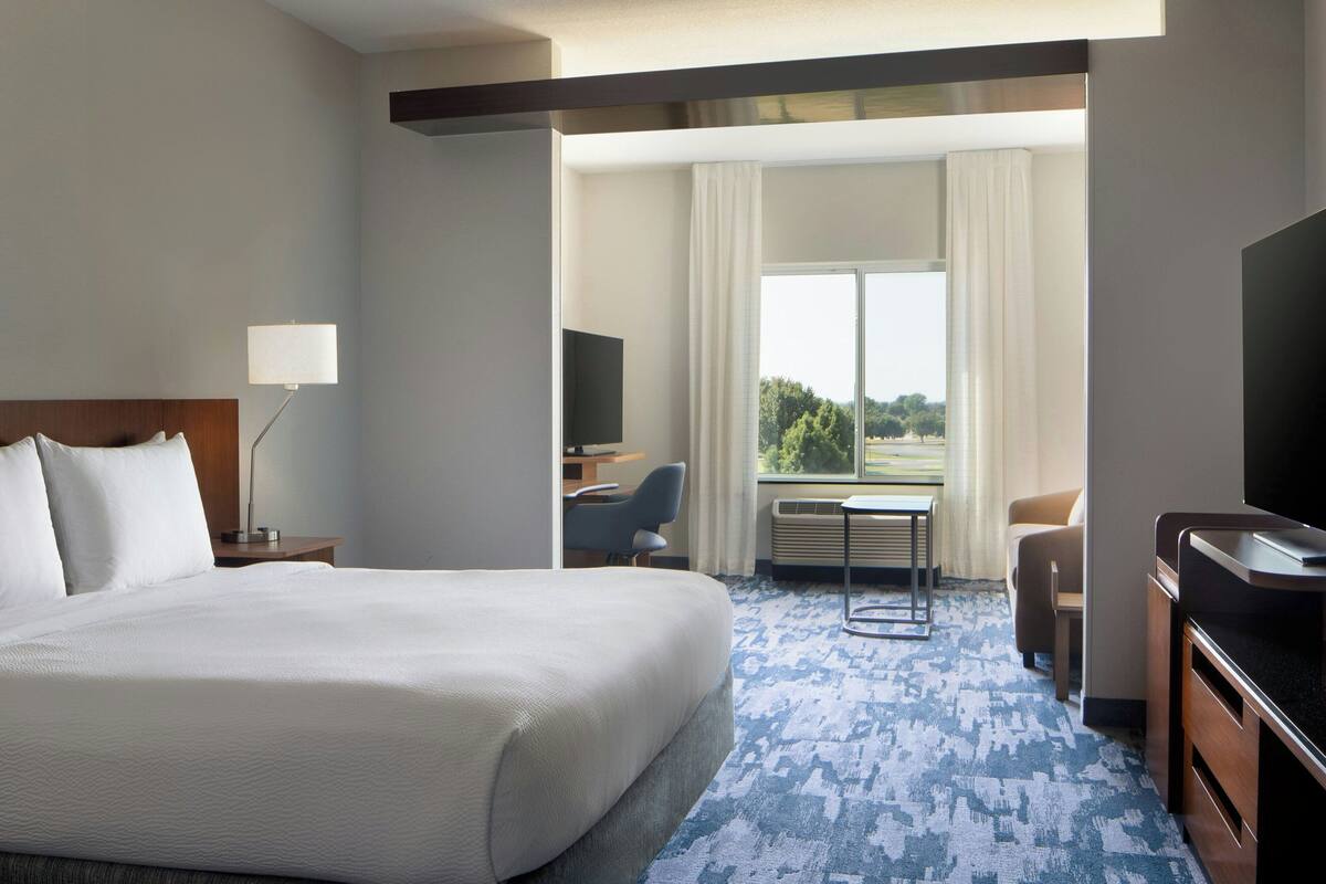 A hotel room with a large bed, a desk, a chair, a television, and a view of the outdoors.