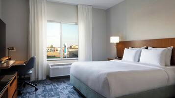 Une chambre d’hôtel avec un grand lit, un bureau, une chaise et une fenêtre avec des rideaux.