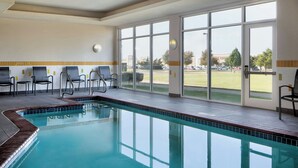 An indoor swimming pool with clear glass walls, a tiled floor, and several chairs along the wall.