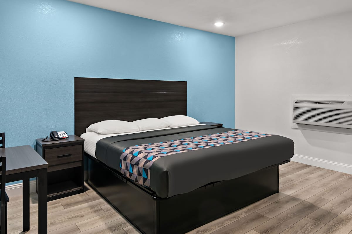 A modern bedroom with a dark headboard, a bed with white pillows, a patterned throw, a bedside table with a phone, and a wall-mounted air conditioner.
