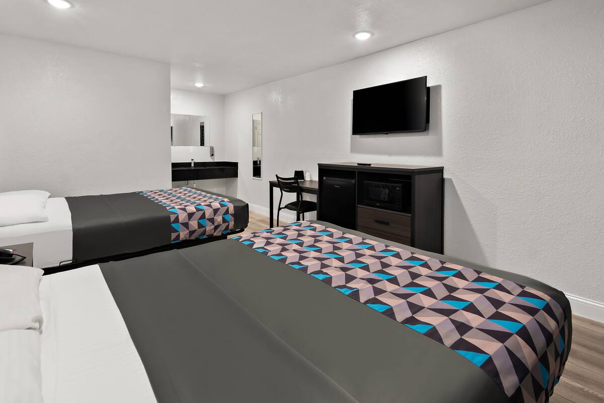 A hotel room with two beds, a TV, a desk, and a mirror.