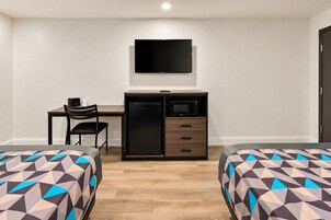 Habitación de hotel con una cama, un escritorio con una silla, televisor, refrigerador y microondas.
