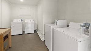 A laundry room with two front-loading washers and a dryer, a wooden table, and a white wall with a window.