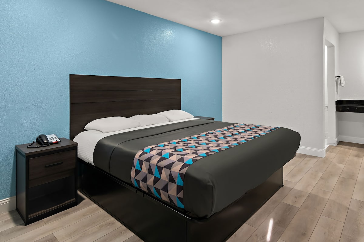 A modern bedroom with a dark wood headboard, a patterned bedspread, a bedside phone, and a small nightstand.