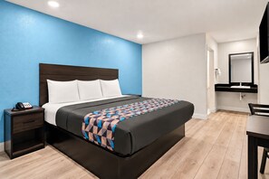 Habitación de hotel con cama, mesita de noche con teléfono, escritorio con silla y espejo sobre el lavamanos.