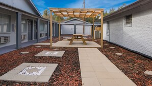A covered patio area with a picnic table, surrounded by a garden with mulch and stepping stones, and adjacent to a building with a garage.