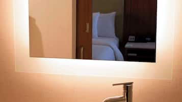 Un baño con un espejo grande, un lavamanos blanco y una puerta de madera.