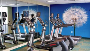 Un gimnasio con cintas de correr, elípticas y un espejo grande.