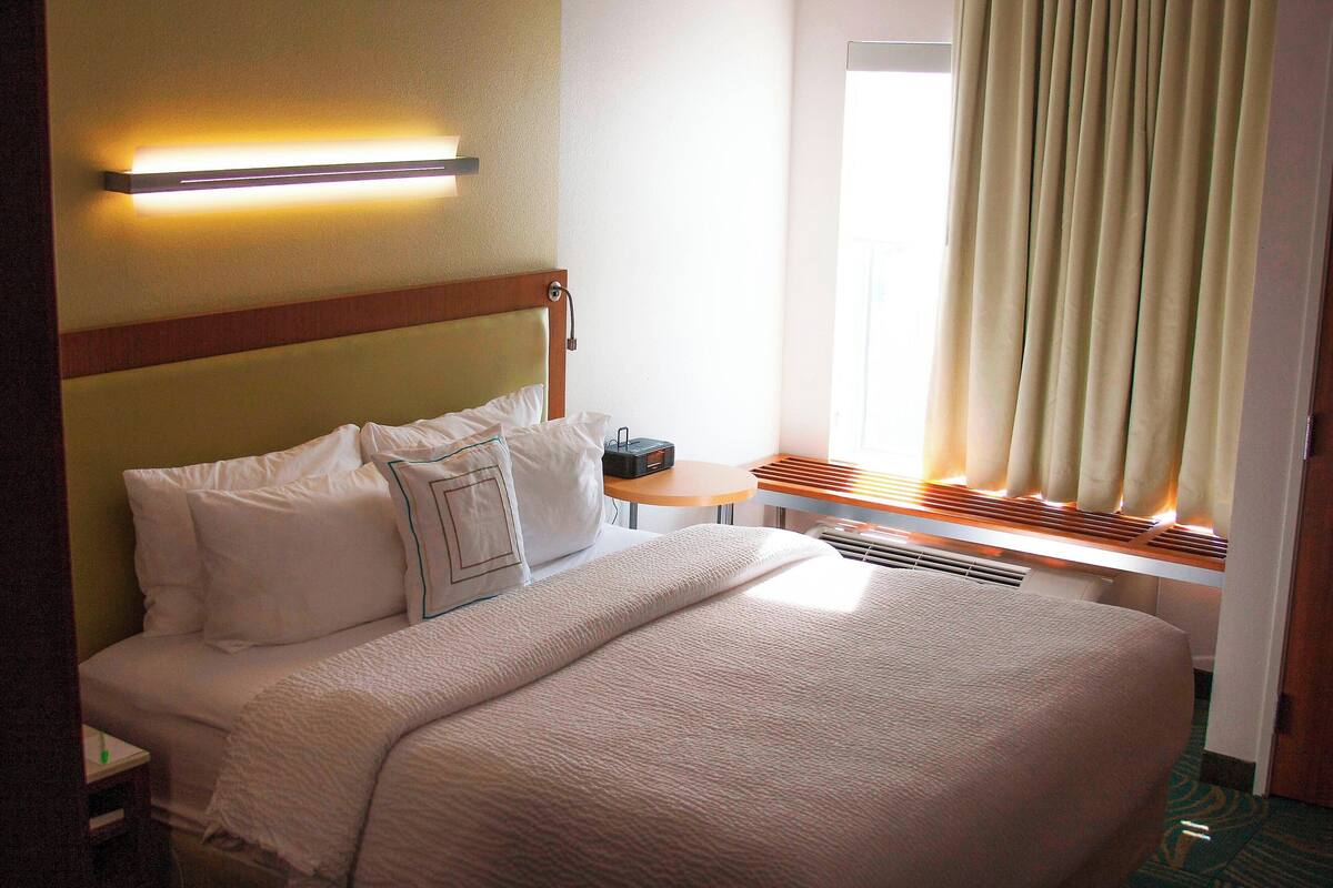 A hotel room with a large bed, a bedside table, a lamp, and a window with curtains.