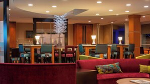 Un moderno hall de hotel con un sofá rojo, una mesa de centro de madera y un comedor con varias sillas y mesas.