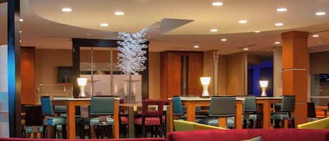 A modern hotel lobby with a red sofa, a wooden coffee table, and a dining area with multiple chairs and tables.