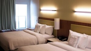Habitación de hotel con dos camas, una mesita de noche con lámpara, un teléfono y una ventana con cortinas.