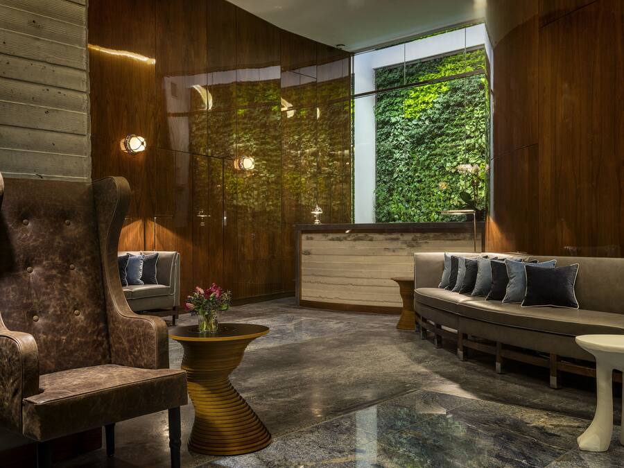 Un hall d’entrée moderne avec un comptoir de réception en bois, un canapé avec des coussins, un fauteuil en cuir et un sol en marbre.