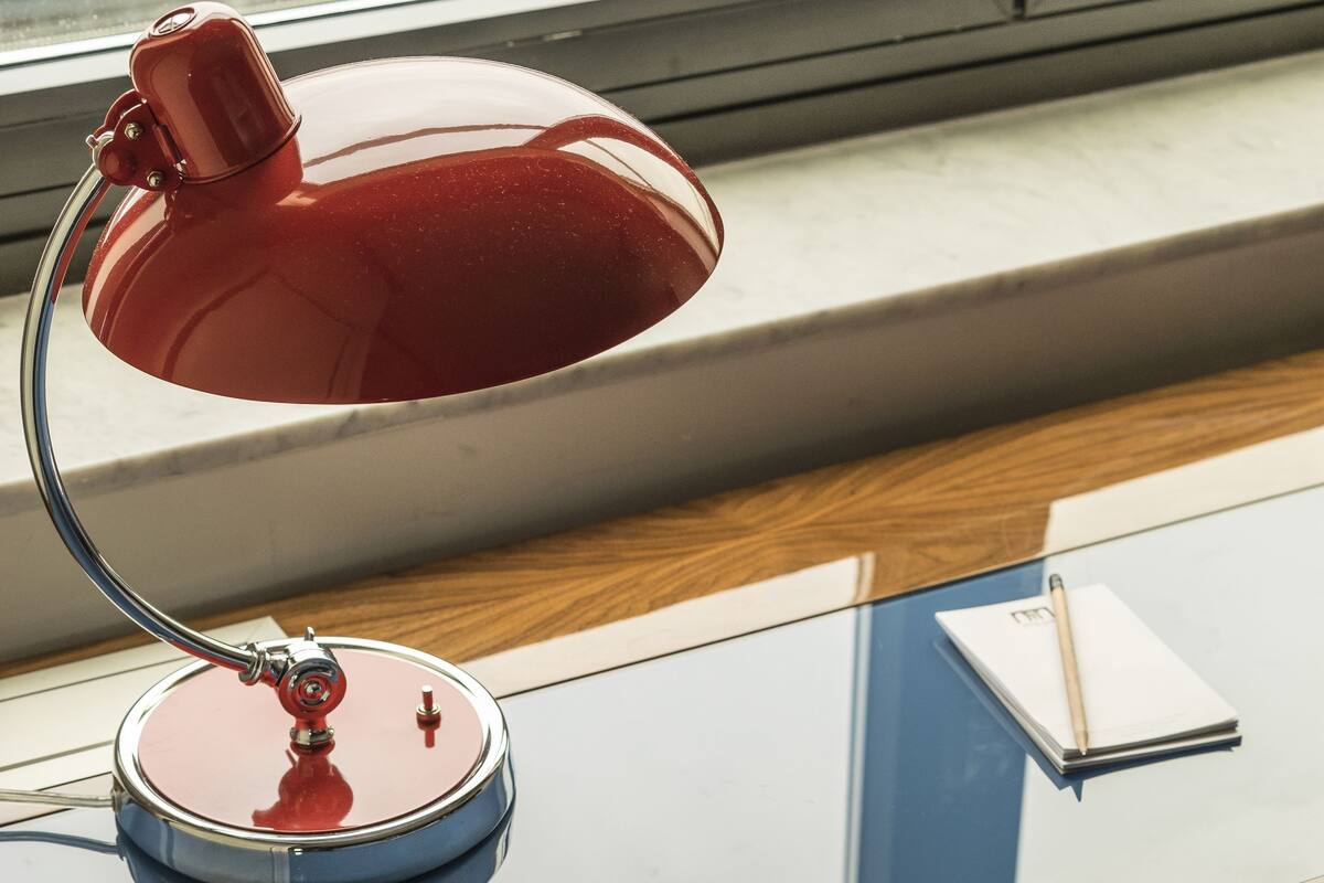 A wooden desk with a red desk lamp, a white notepad, and a pen.