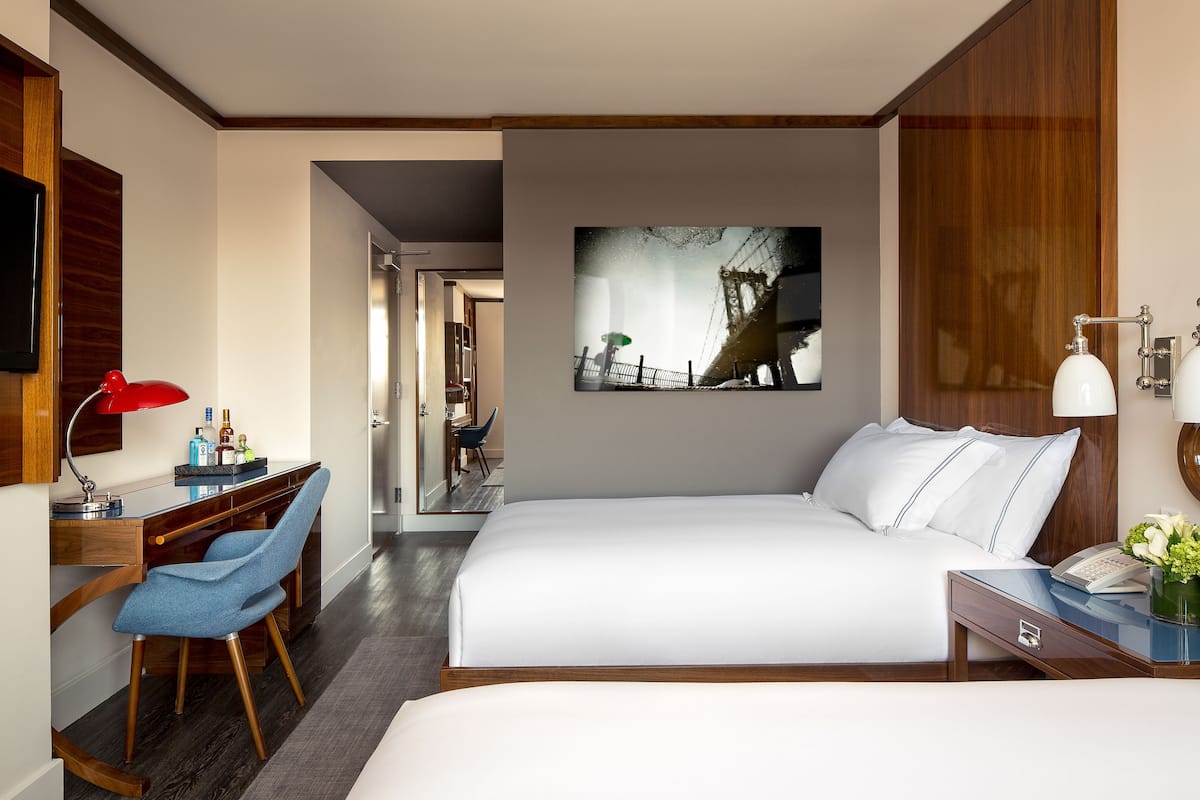 A hotel room with a bed, a desk with a chair, a TV, and a painting on the wall.