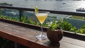 Un cocktail sur une table en bois, avec une vue sur les gratte-ciel de la ville et une rivière en arrière-plan.
