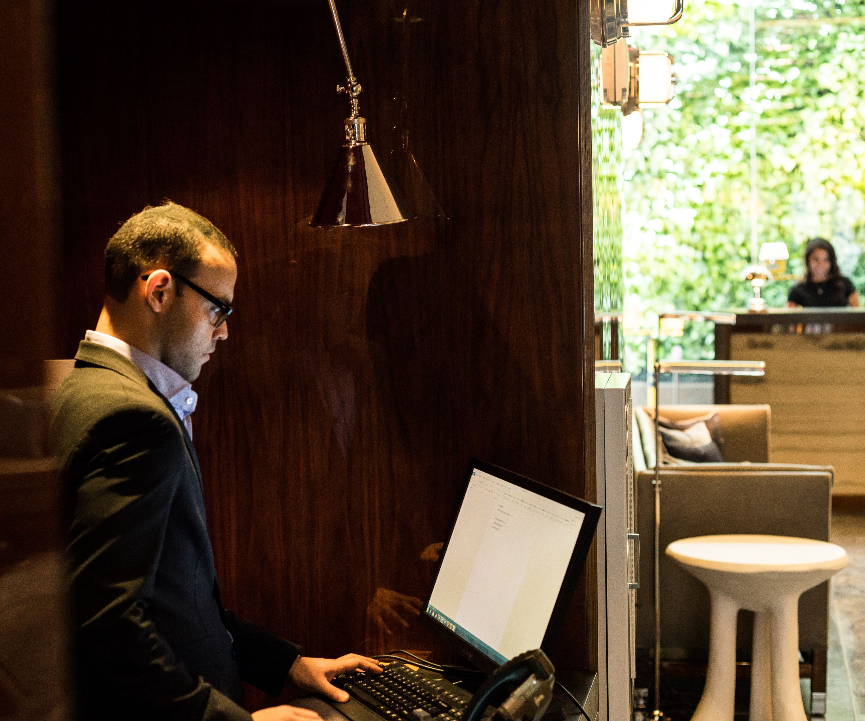A man working on a laptop in a room with a wooden wall and a reception desk in the background.