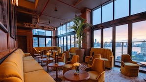 Un hall d’hôtel situé dans un immeuble de grande hauteur, avec un grand espace salon, une plante en pot et une vue sur la ville à travers de grandes fenêtres.