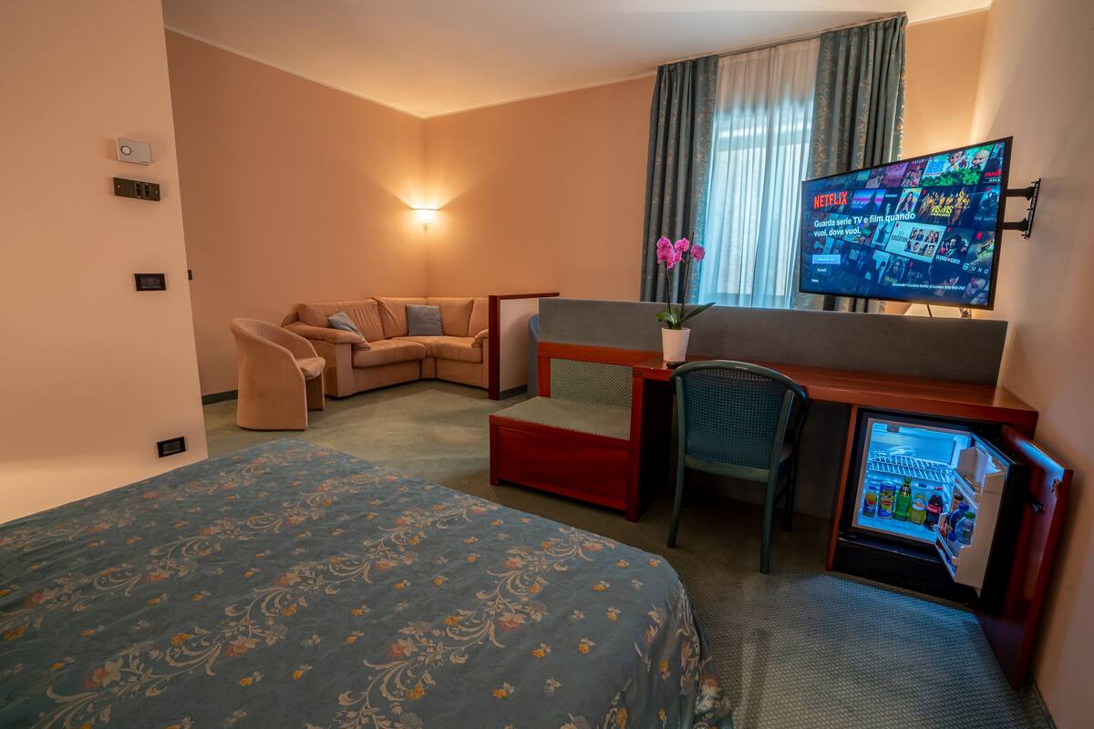 A hotel room with a bed, a sofa, a desk with a computer, a TV, and a mini-fridge.