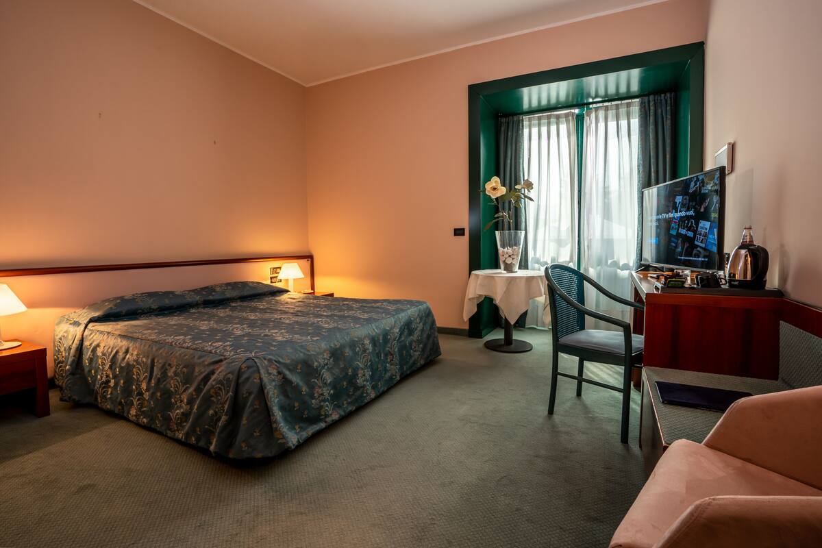 A hotel room with a bed, a desk, a chair, a TV, and a window with curtains.