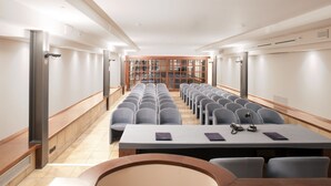 A conference room with rows of chairs, a long table, and a view of a library through glass doors. - Hotel Diana (Valdobbiadene)