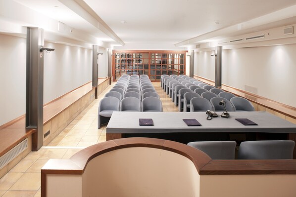 A conference room with rows of chairs, a long table, and a view of a library through glass doors.