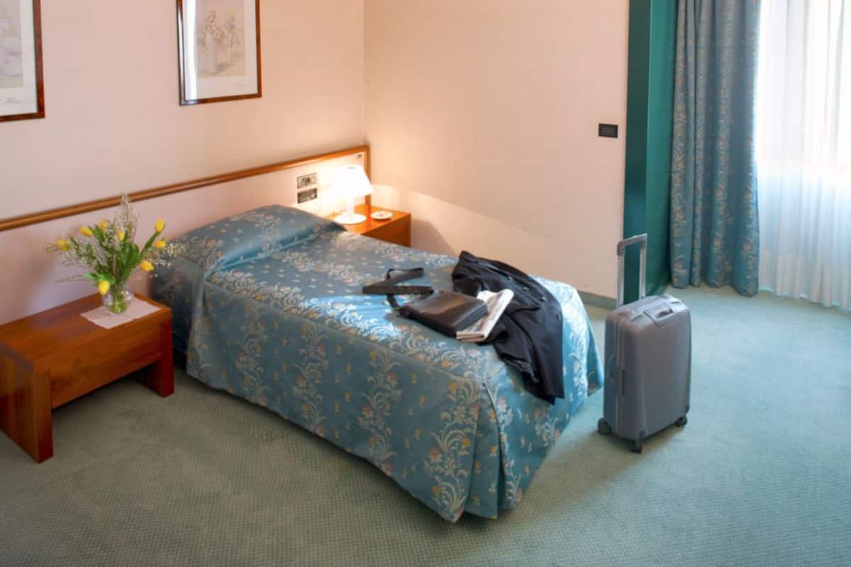 A hotel room with a bed, bedside table, lamp, and a suitcase.