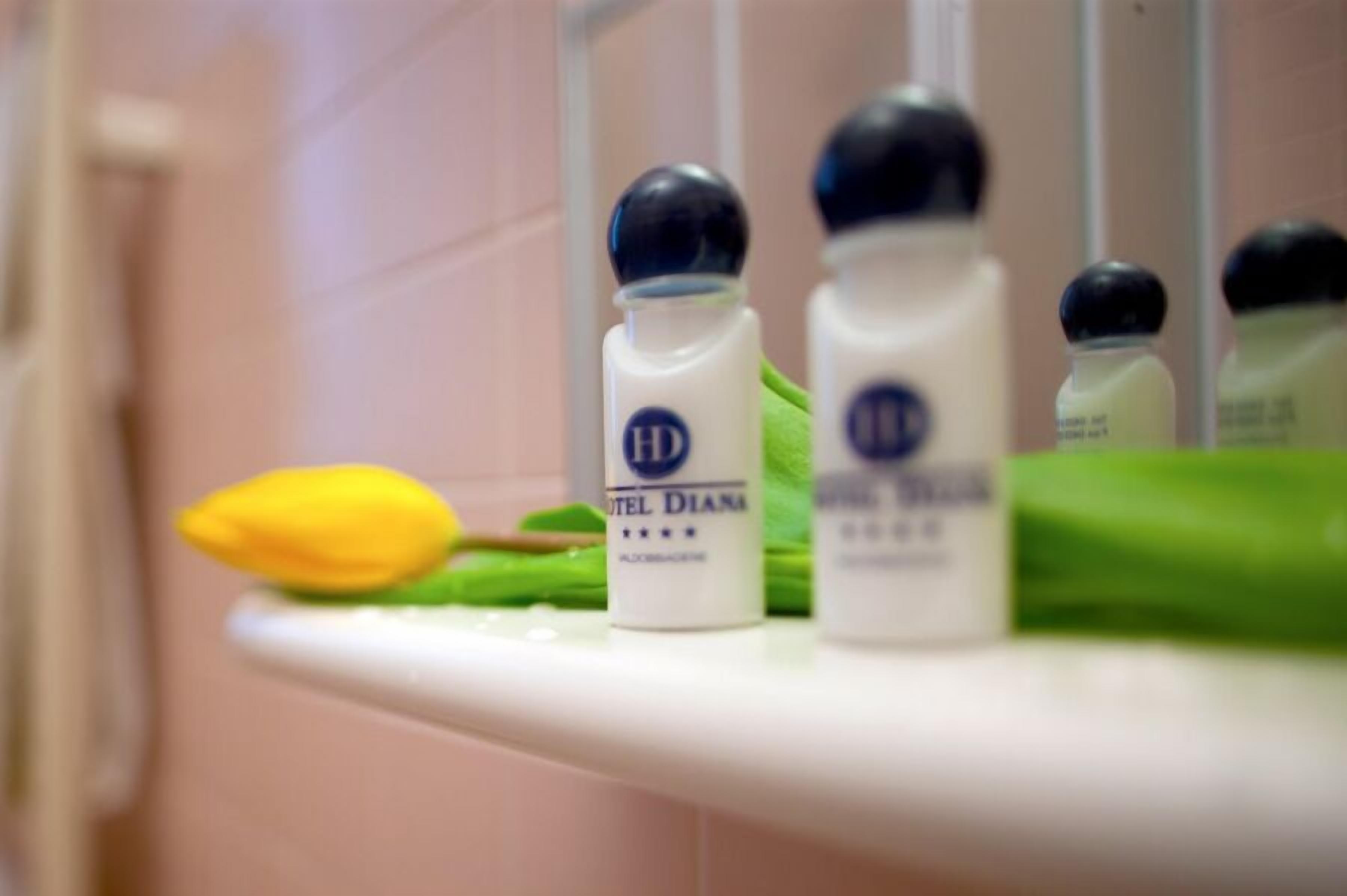 A bathroom shelf with three bottles labeled 'Hotel Diana' and a yellow flower.