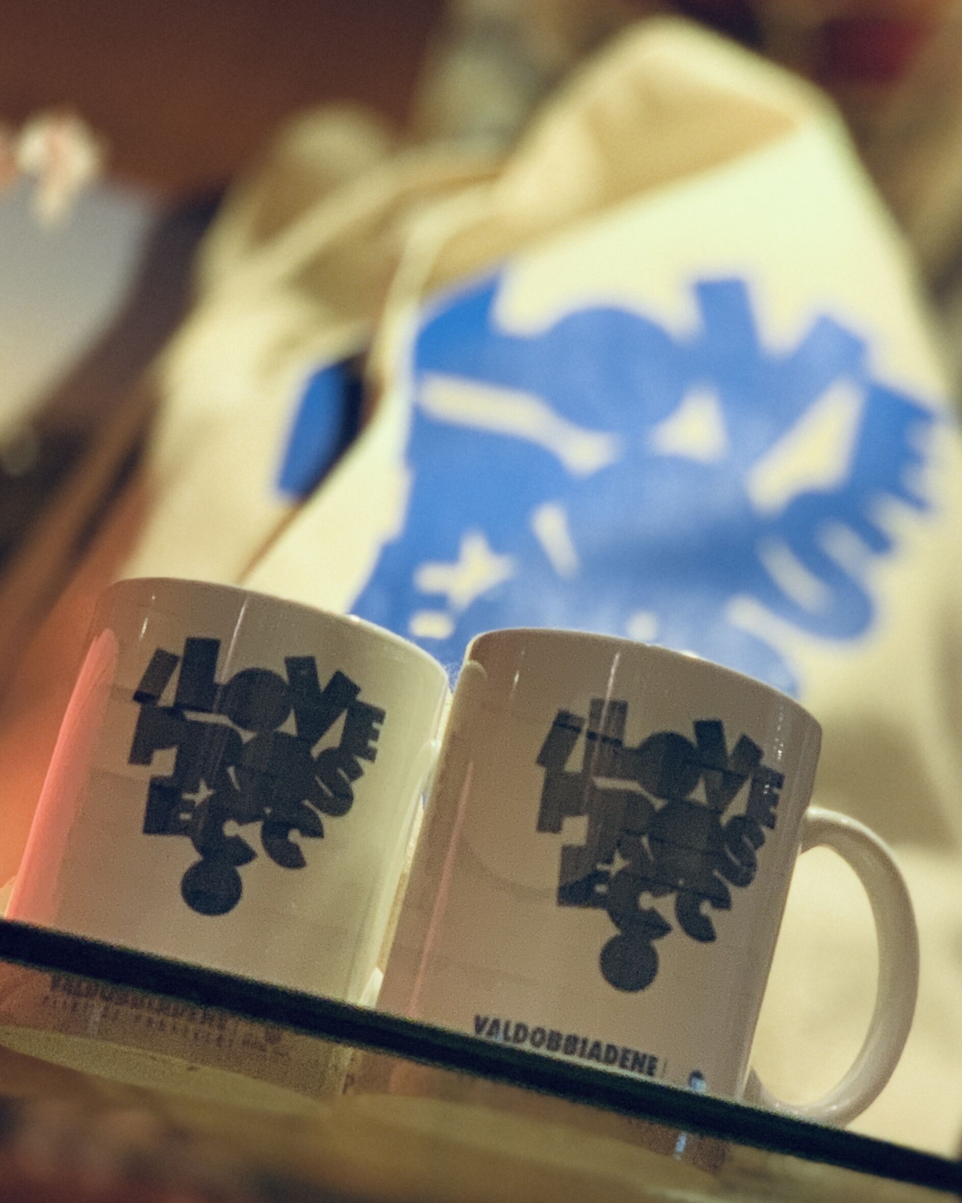 Two white mugs with black text on a shelf.