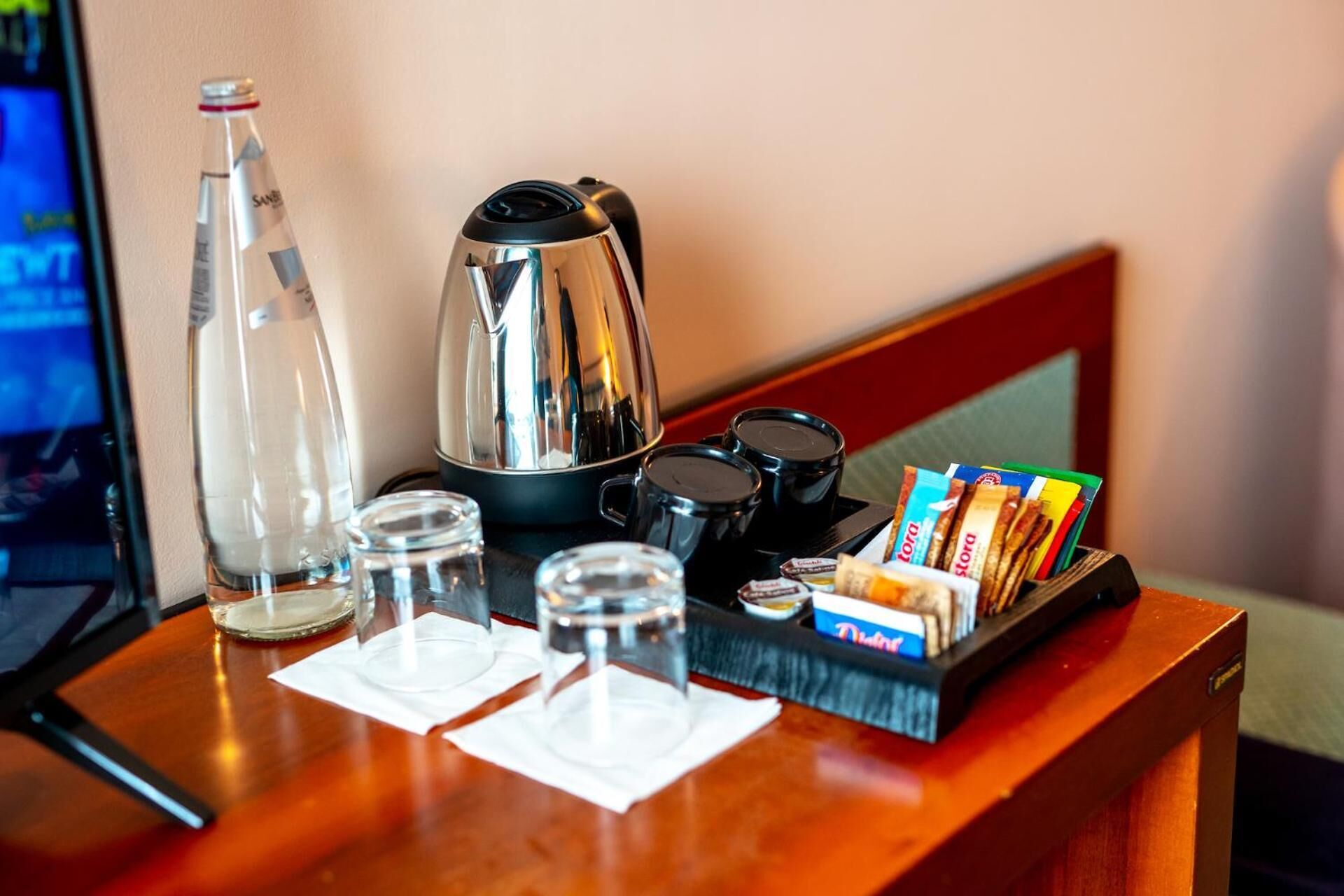 A hotel room's reception area with a coffee maker, a bottle of water, glasses, and a tray with snacks and a magazine.