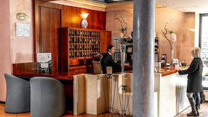 A reception area with a wooden reception desk, a large vase with flowers, and a wall-mounted display of framed certificates. - Hotel Diana (Valdobbiadene)