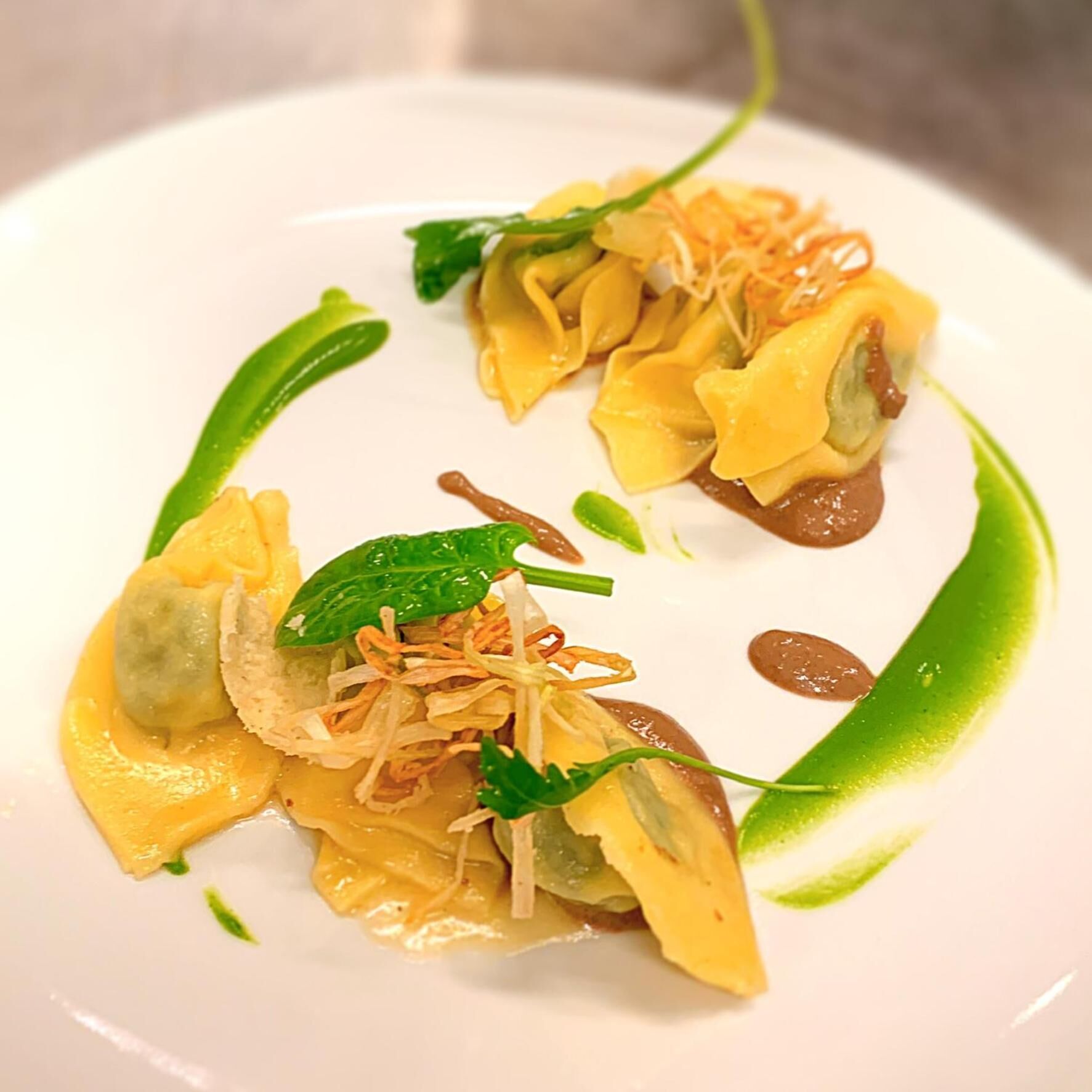 A plate of ravioli with a green sauce and garnishes.