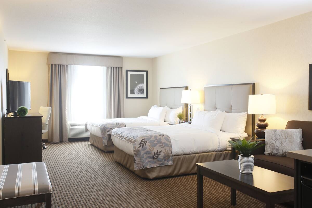 A hotel room with two beds, a desk, a chair, a TV, and a window with curtains.