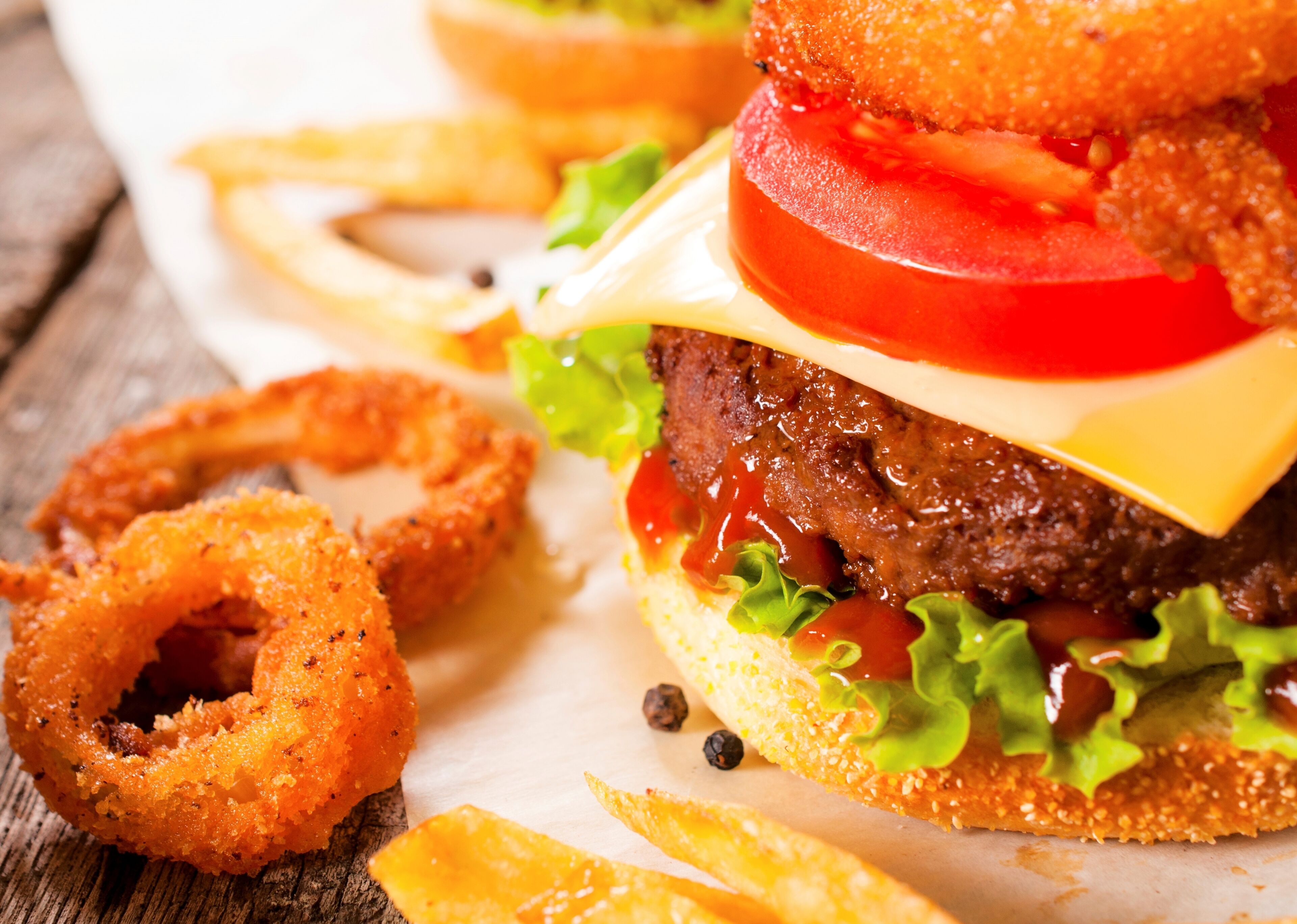 A close-up of a burger with lettuce, tomato, cheese, and a beef patty, accompanied by onion rings and fries.