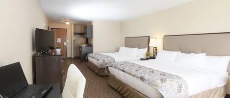 A hotel room with two beds, a desk with a laptop, a TV, and a small kitchenette.