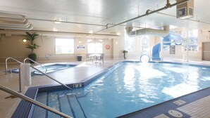 An indoor swimming pool with a diving board, a slide, and a seating area with chairs.