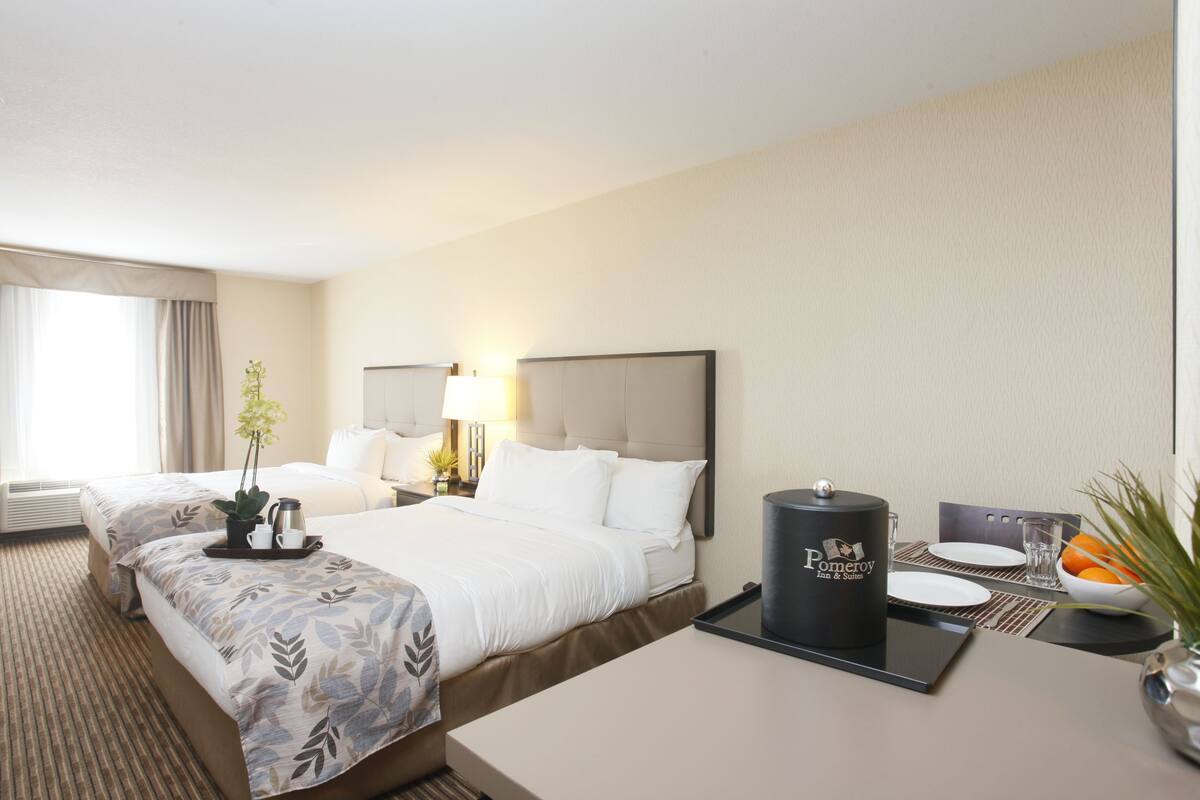 A hotel room with two beds, a dining table, a coffee maker, and a vase with flowers.