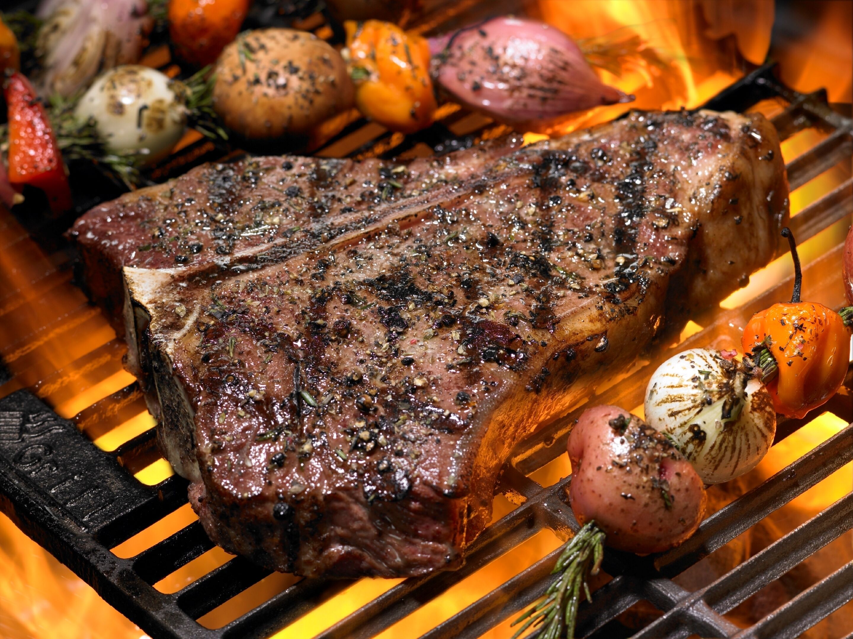 A steak grilling on a barbecue with vegetables.