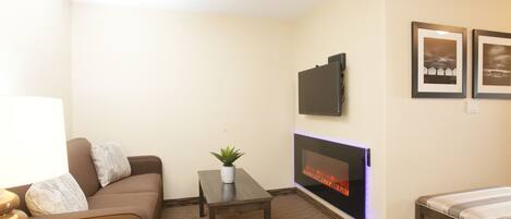 A modern living room with a sofa, a small table with a plant, a flat-screen TV mounted on the wall, and a fireplace.