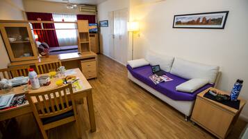 Una habitación de hotel funcional con una mesa de comedor de madera, un sofá con funda morada, un armario pequeño y una cama.