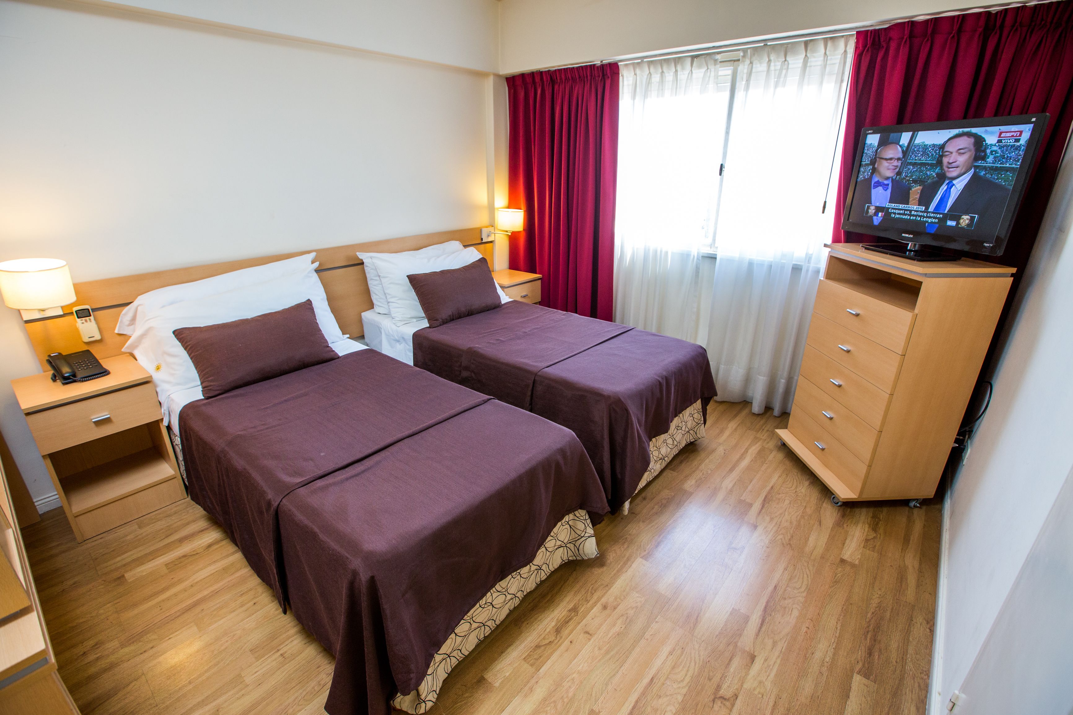 Een hotelkamer met twee bedden, een televisie, een houten dressoir en een nachtkastje met een lamp.